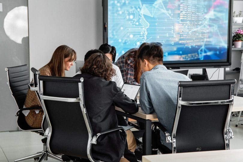 Profissionais reunidos em mesa com laptop mostrando diagrama de fluxo de chatbot e ícone do WhatsApp